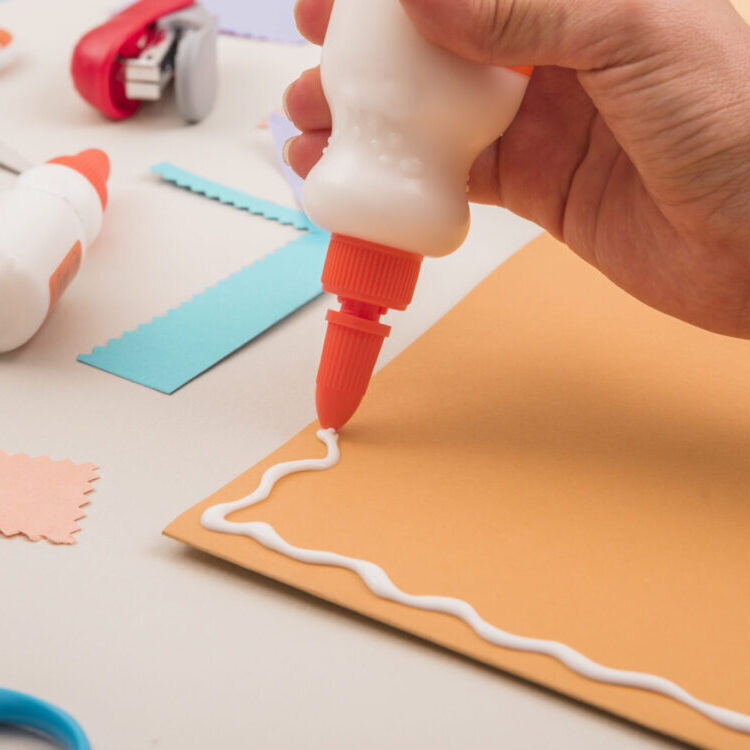 human-hand-applying-white-glue-orange-paper-with-scissor-stapler human-hand-applying-white-glue-orange-paper-with-scissor-stapler